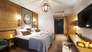 Habitación de hotel con dos camas, paneles de madera, un cuadro grande, un televisor y una cesta de frutas.
