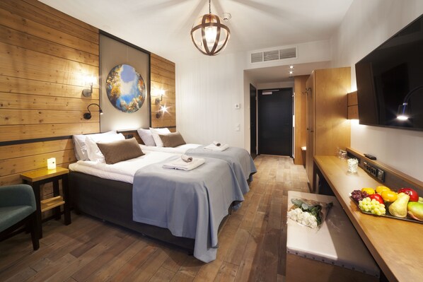 A hotel room with two beds, wooden paneling, a large painting, a TV, and a fruit basket. - Hotel Aateli Hillside (Sotkamo)