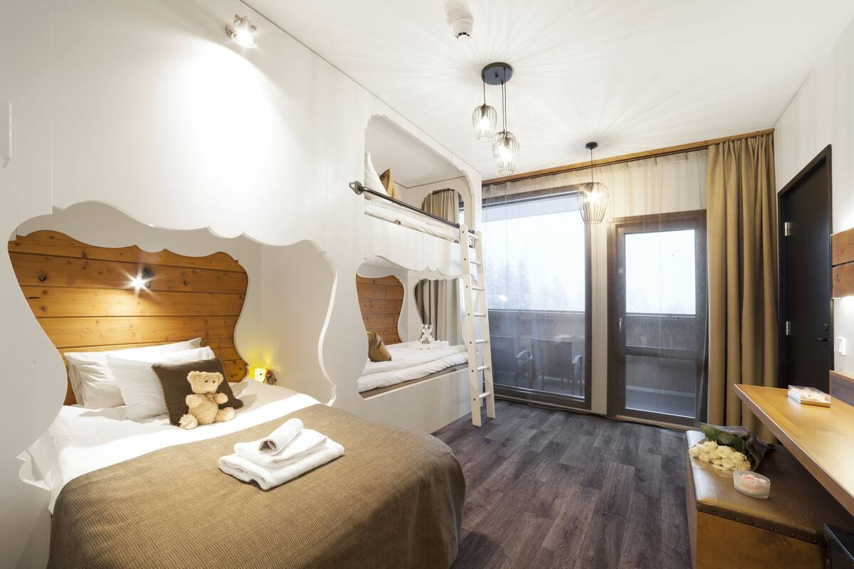Ein Hotelzimmer mit Etagenbett, Schreibtisch, Stuhl, Fernseher und einem Balkon mit Blick.