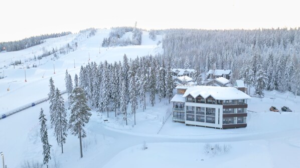 A snow-covered lodge with a modern architectural style, surrounded by dense forest and a ski slope. - Hotel Aateli Hillside (Sotkamo)
