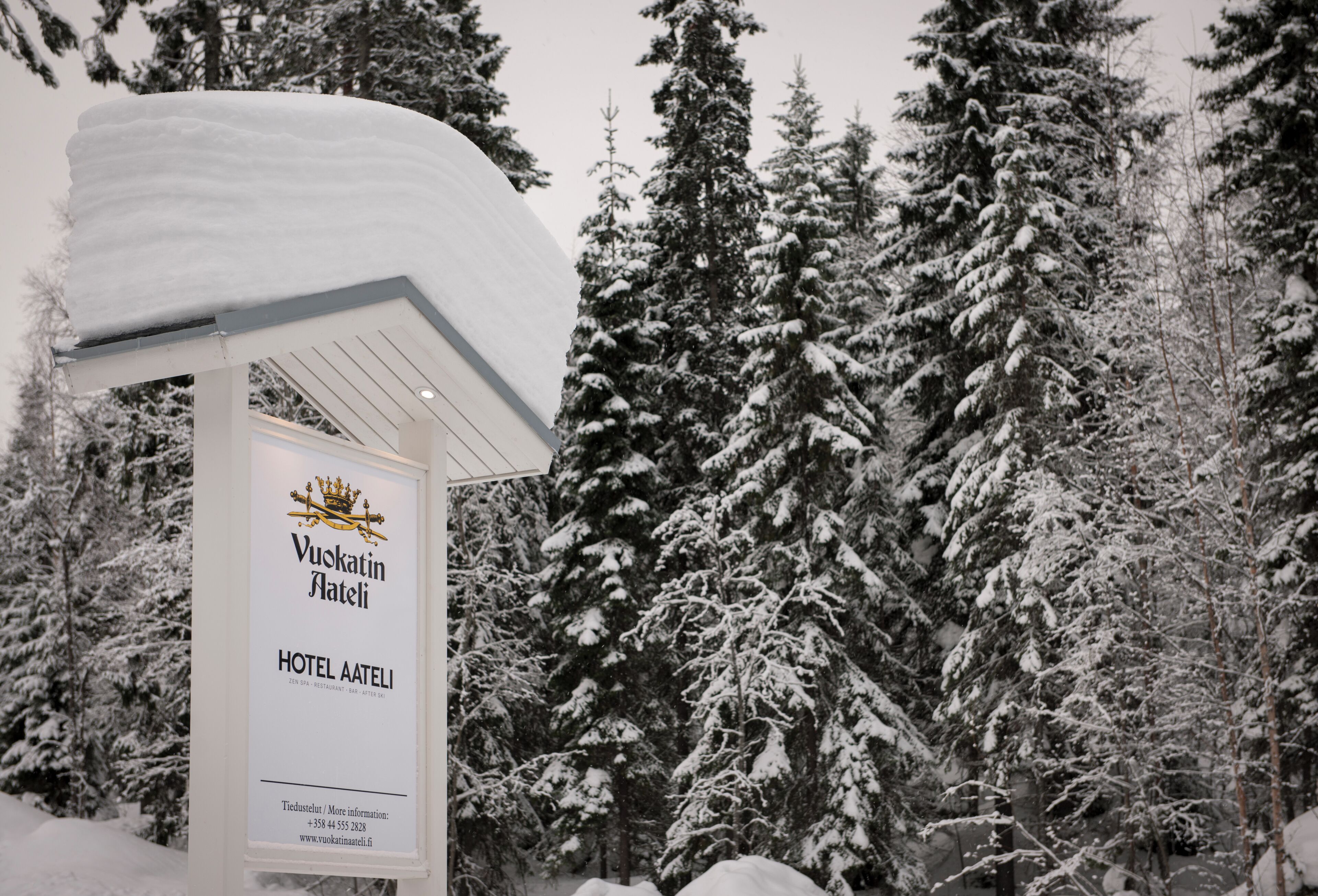 Un letrero de hotel cubierto de nieve con el nombre 'Vuokatin Aateli' e información de contacto.