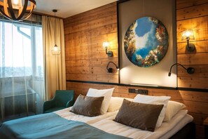 A hotel room with a wooden wall, a bed with pillows, a chair, and a painting.