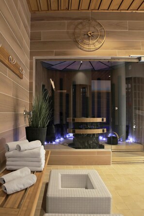 Un espacio moderno de spa con un banco de madera, una zona de estar con toallas, un reloj decorativo grande y una partición de vidrio.