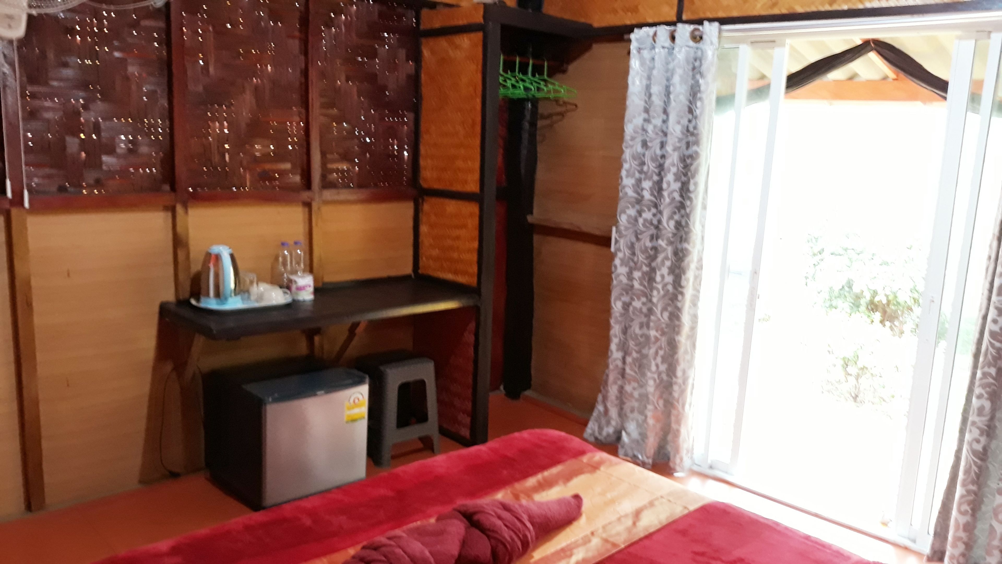 A room with a bed, a desk, a small refrigerator, and a window with curtains.