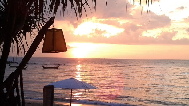 Une scène de plage au coucher du soleil, avec deux chaises de plage, une table et une lampe.