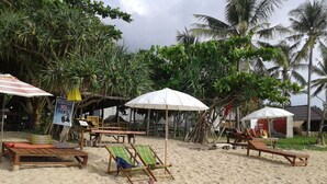 Une plage avec des chaises longues en bois, des parasols et un panneau indiquant un service de location de motos.