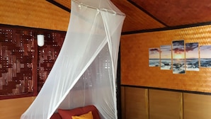 Une chambre avec un lit, des coussins rouges et jaunes, une moustiquaire et un mur orné d’un motif tissé et de tableaux.