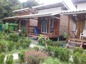 Una casa de madera con porche, rodeada de un jardín lleno de plantas y flores.