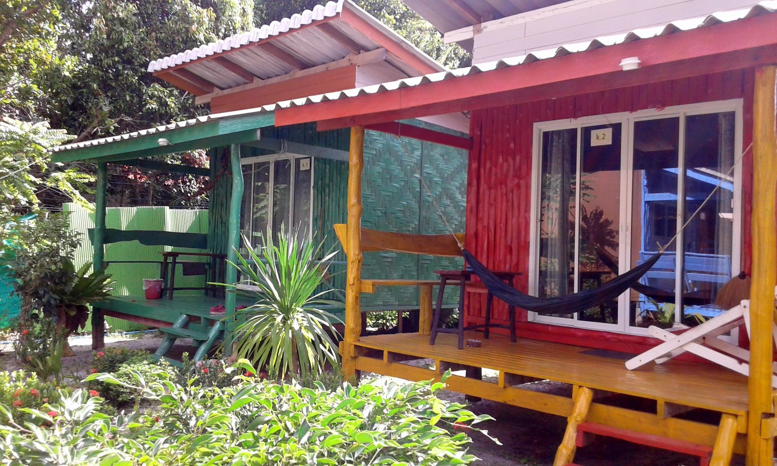 A small, colorful wooden structure with a porch, a hammock, and a bench.
