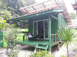 Una estructura verde de madera con un porche, una hamaca y una pequeña mesa.