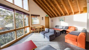 A modern interior with a high ceiling, large windows, and a seating area with sofas and a table. - Terama Ski Lodge (Mount Buller)