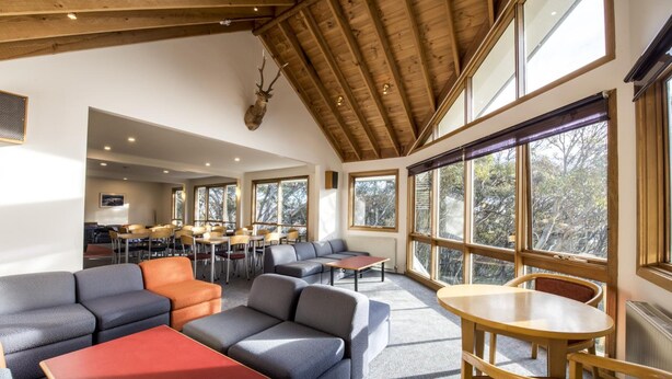 A spacious room with a high ceiling, large windows, and a variety of seating arrangements including sofas and tables. - Terama Ski Lodge (Mount Buller)