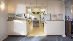 A modern kitchen with white cabinets, a central island, and a built-in oven. - Terama Ski Lodge (Mount Buller)