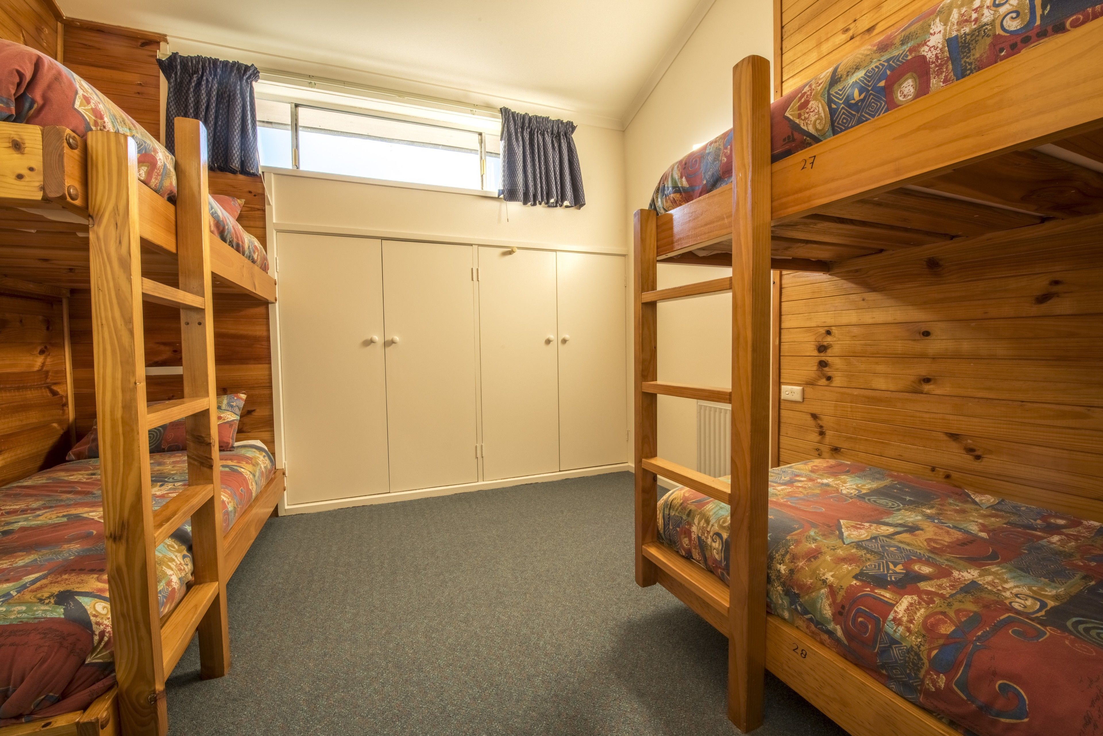 A dormitory room with bunk beds, a wardrobe, and a window with curtains.