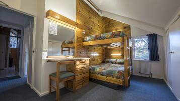 Une chambre avec un lit superposé, un bureau et une chaise, des murs en bois, une fenêtre et un radiateur.