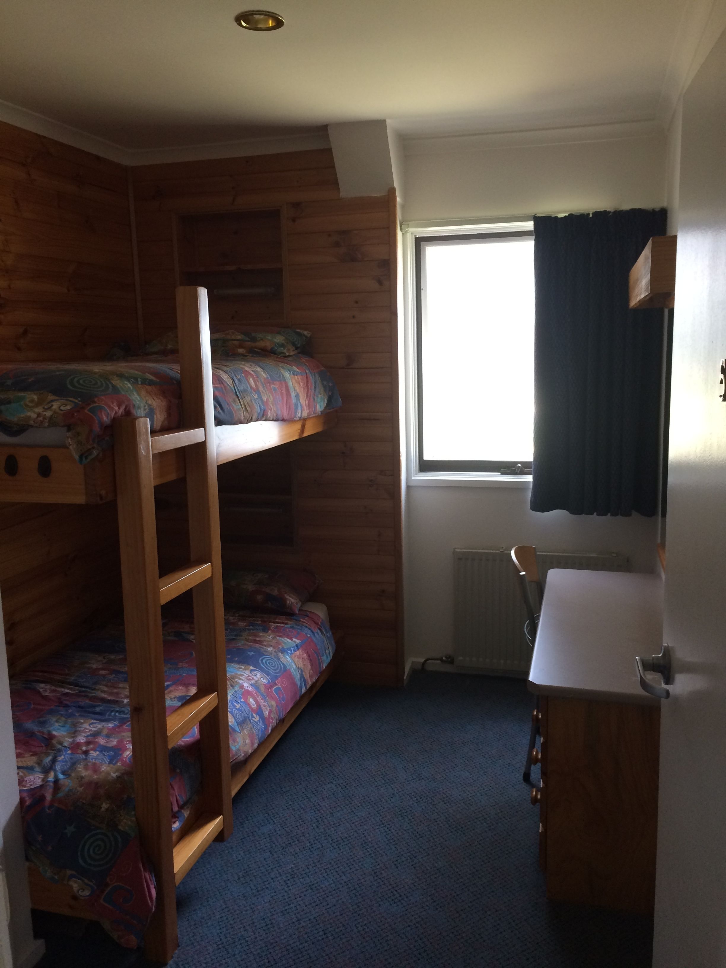 Une chambre avec un lit superposé, une fenêtre, un radiateur et un petit lavabo.