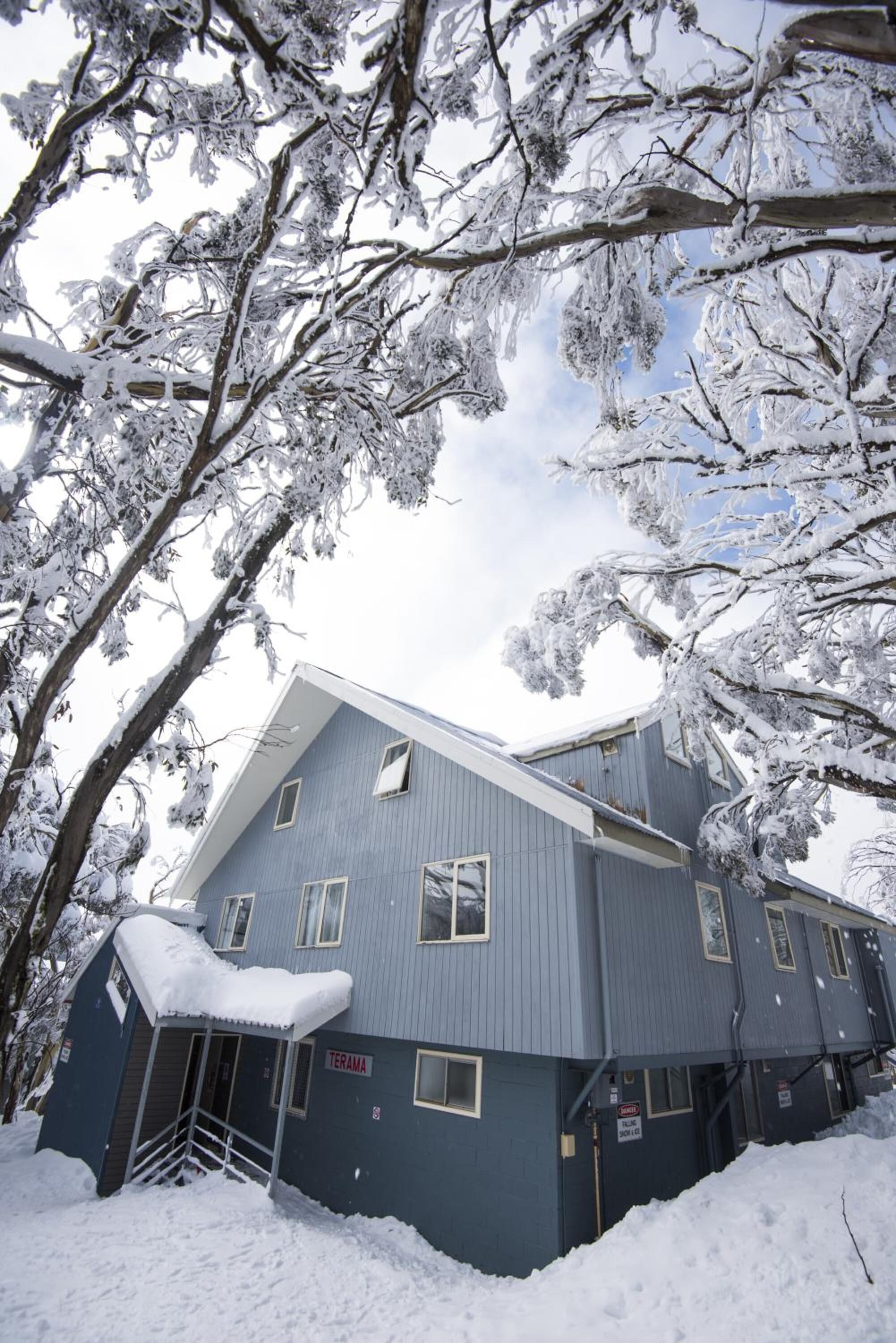 A two-story building with a sloped roof, surrounded by snow-covered trees.