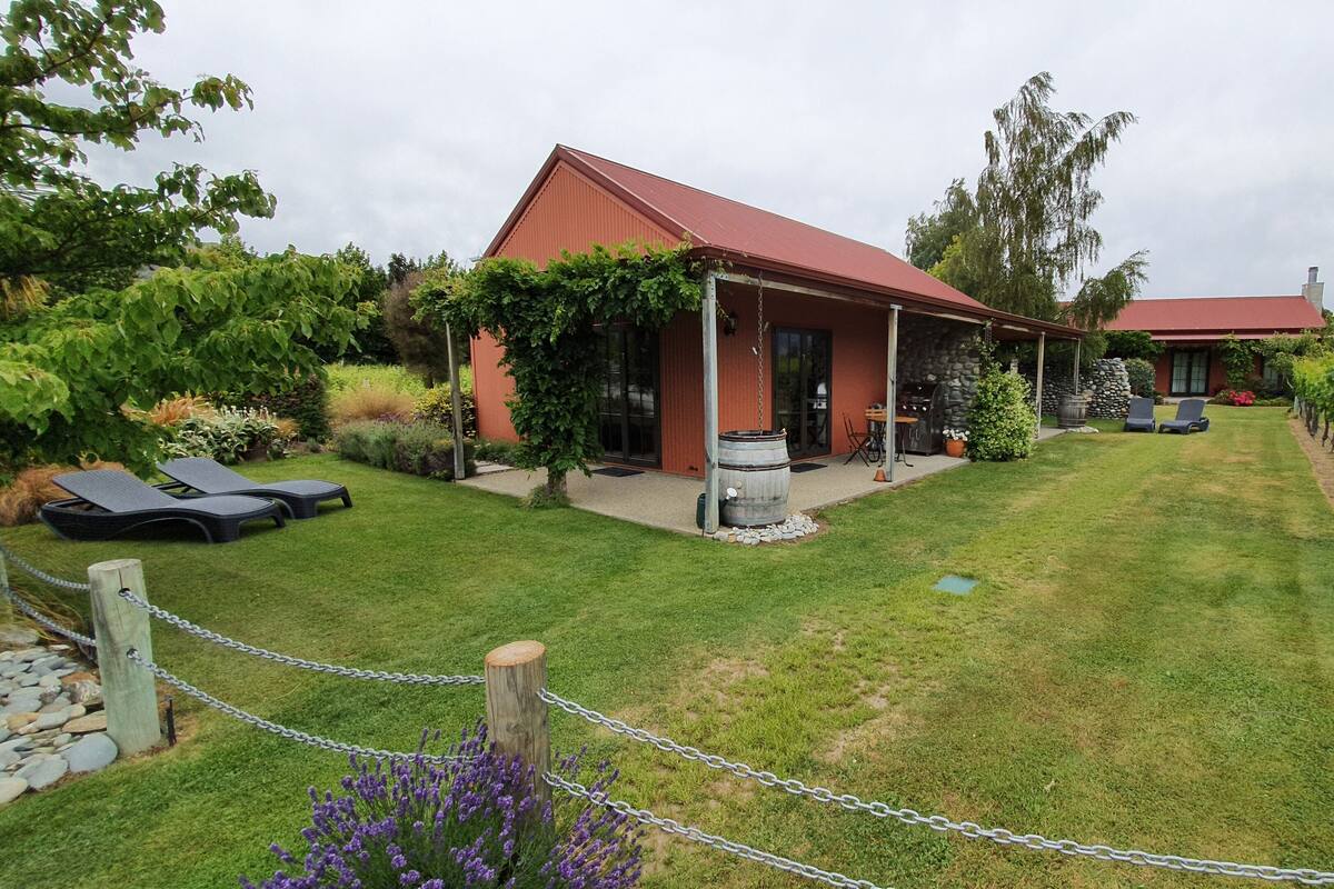 A house with a red roof, a covered porch, and a vineyard in the background.