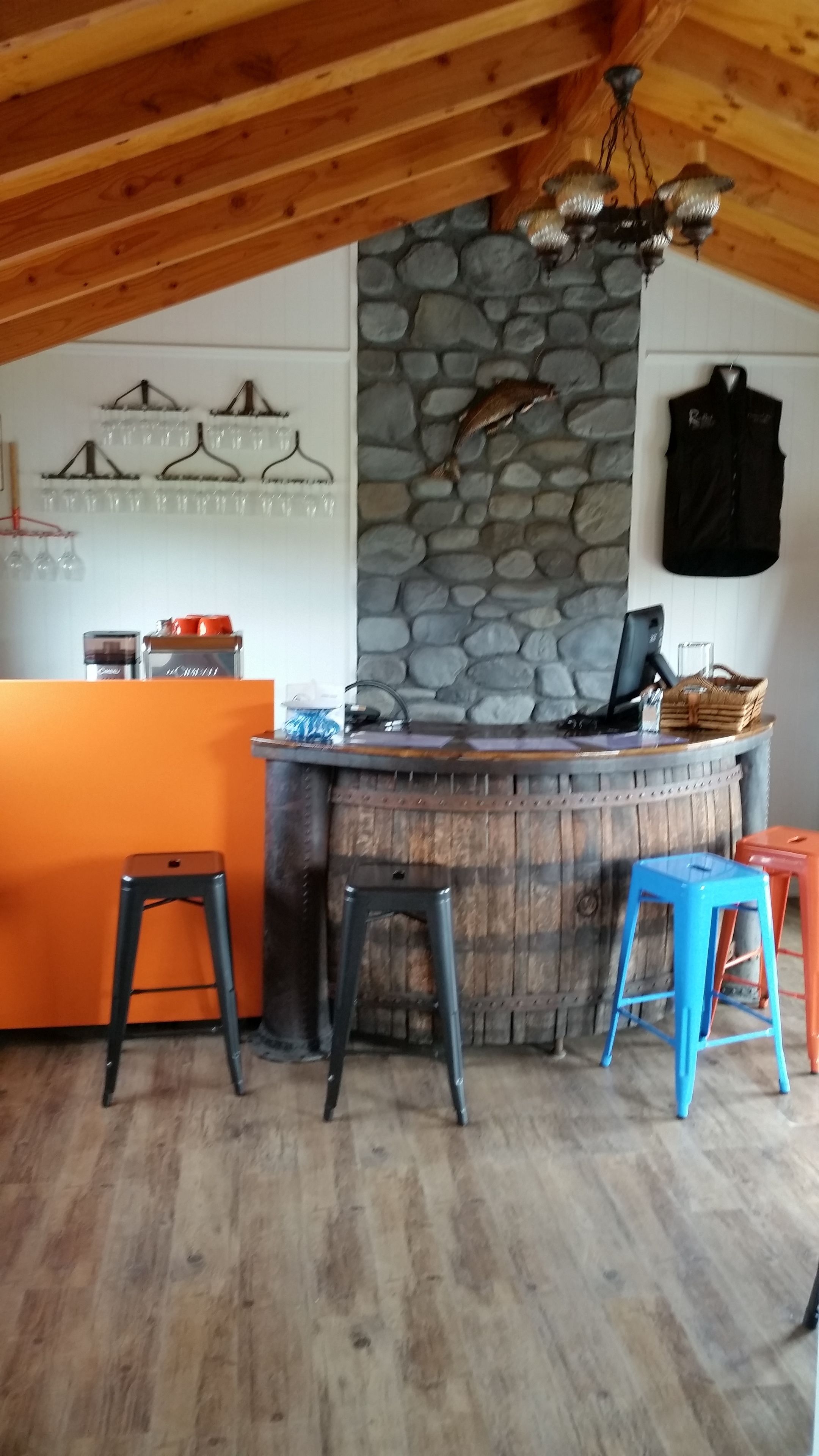 A rustic bar area with a stone wall, wooden ceiling, and stools.