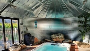 Un jacuzzi con un deck de madera alrededor, techo metálico y vistas al exterior a través de amplios ventanales.