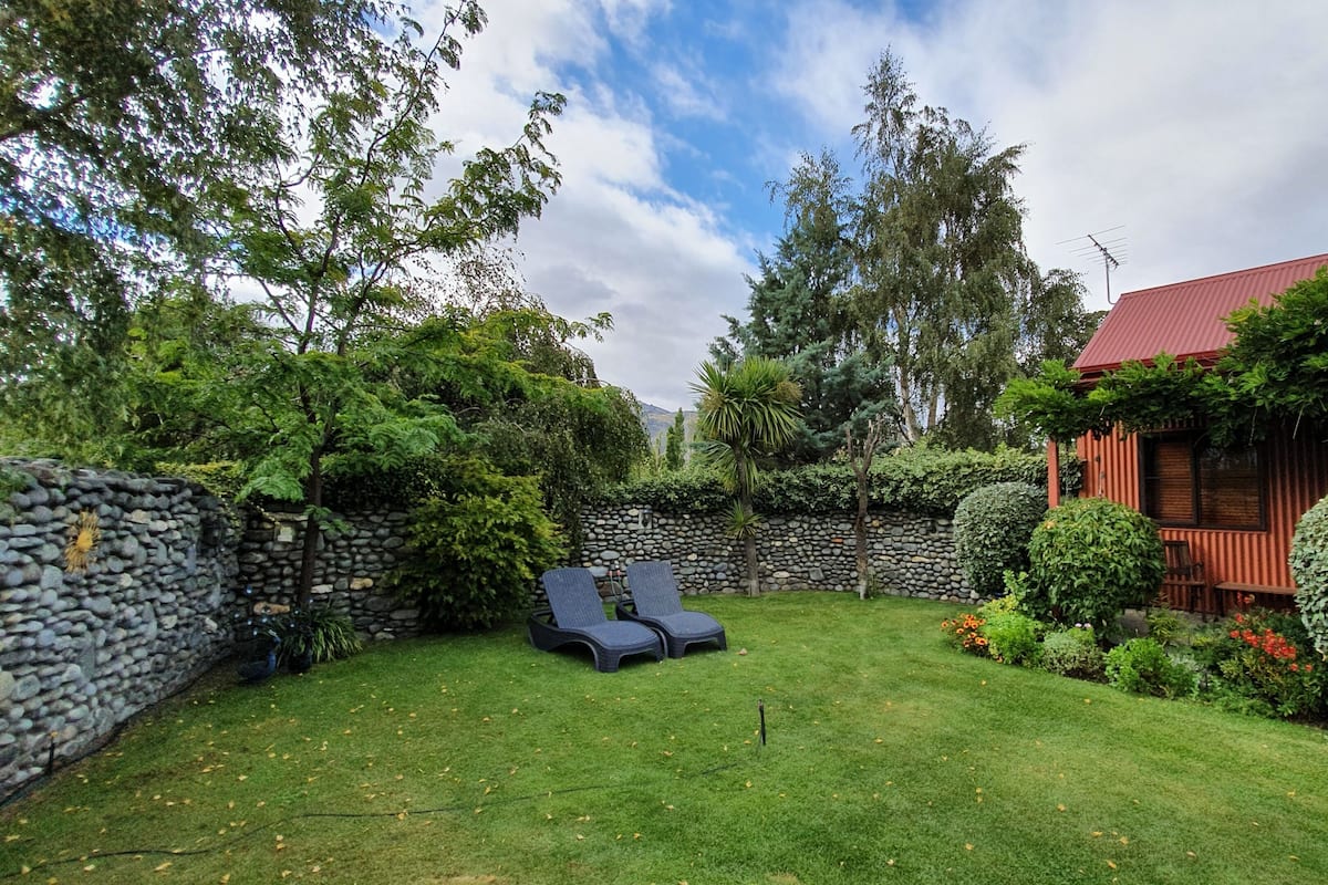 A well-maintained garden with a stone wall, a wooden cabin, and a lounge chair.