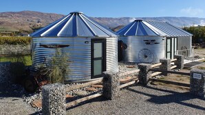 Dos estructuras con techo metálico identificadas como 'Spa House' y 'Pool House' en un entorno rural con montañas al fondo.