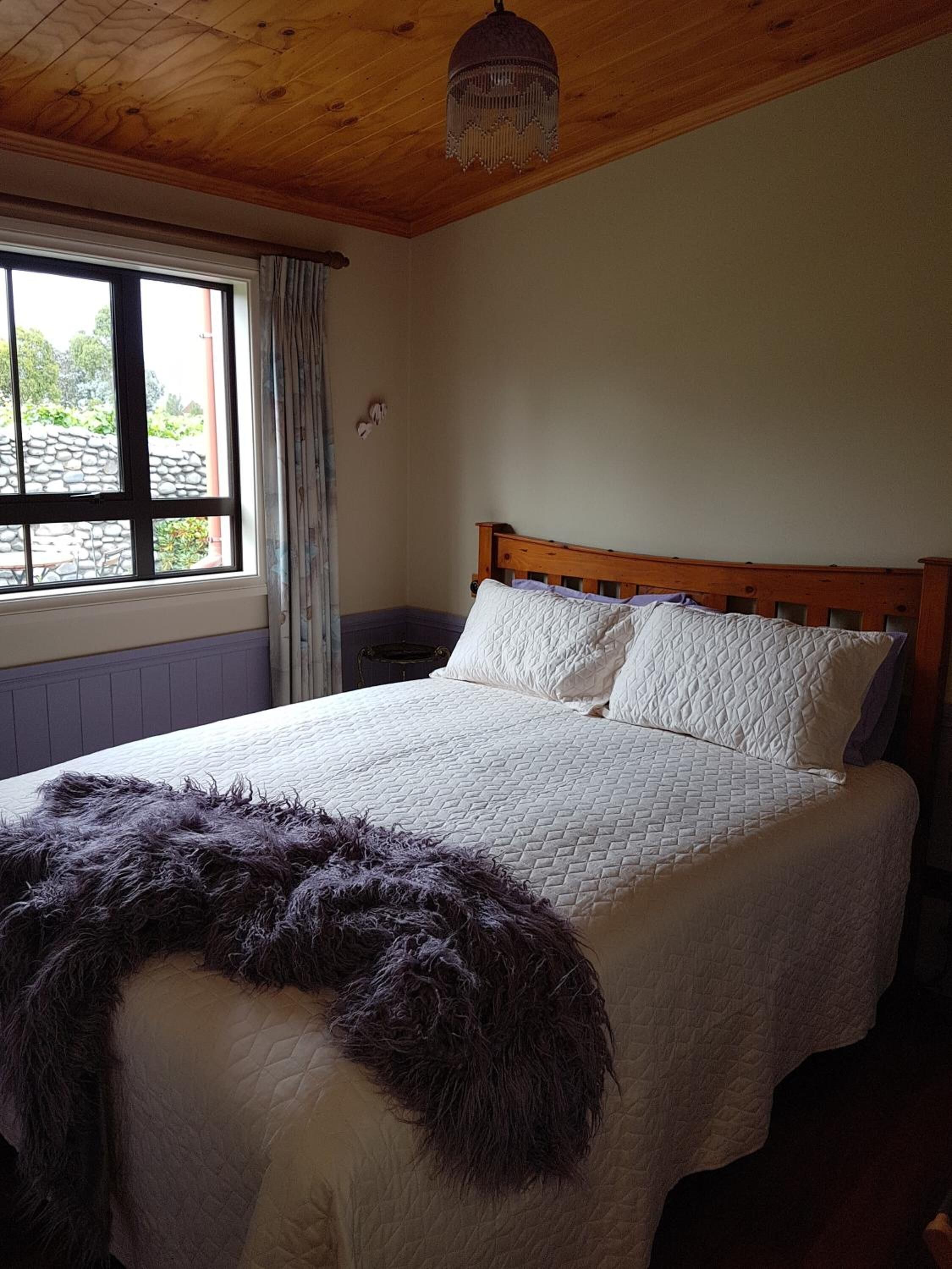 Un dormitorio con cama de madera, una ventana con cortinas y techo de madera.