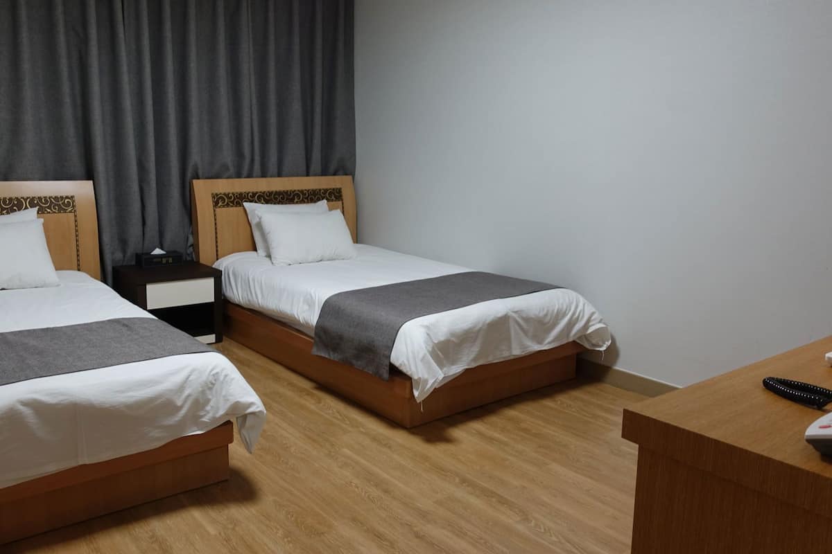 A hotel room with two beds, a bedside table with a lamp, a desk with a phone, and a curtain.