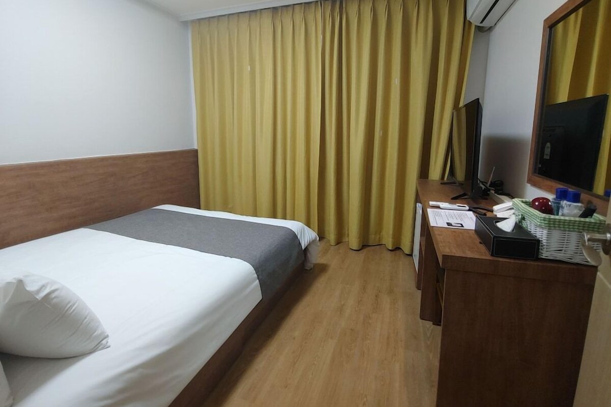 Une chambre d’hôtel avec un lit, un bureau, une télévision et une fenêtre avec des rideaux.