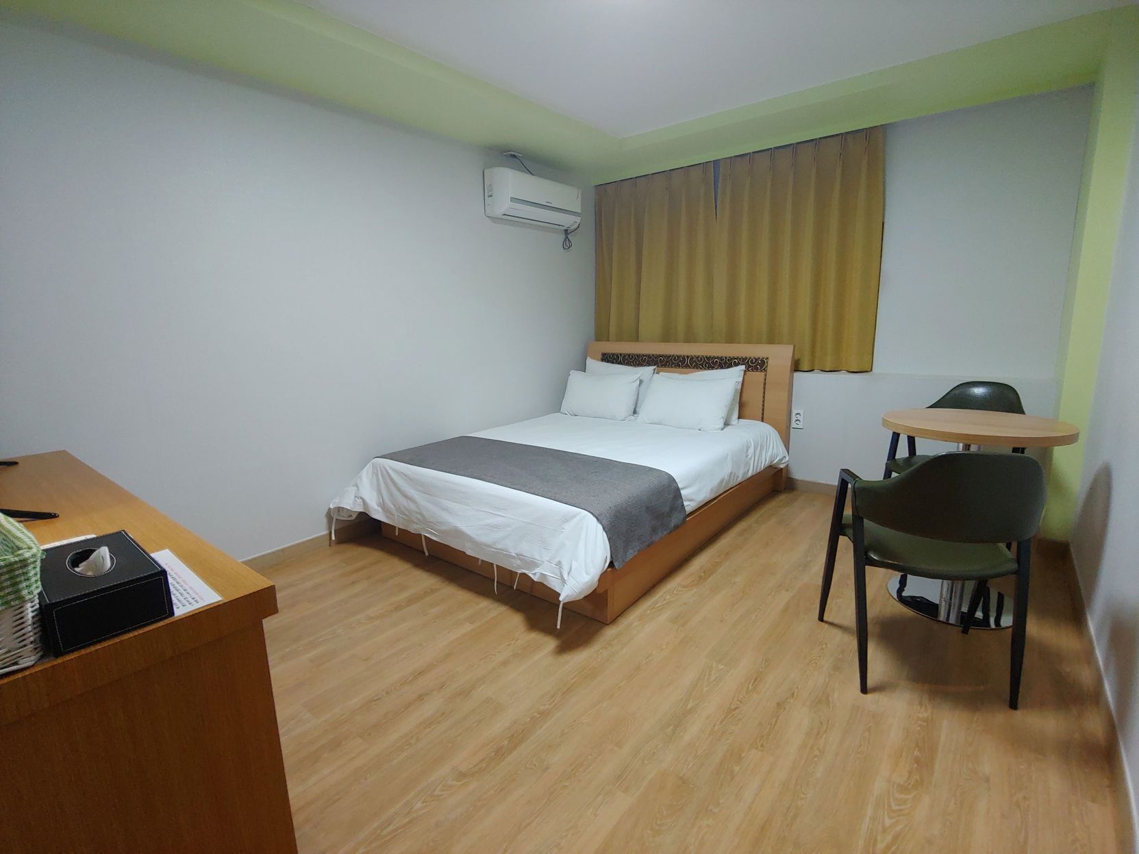 A hotel room with a bed, a desk, a chair, and an air conditioning unit.