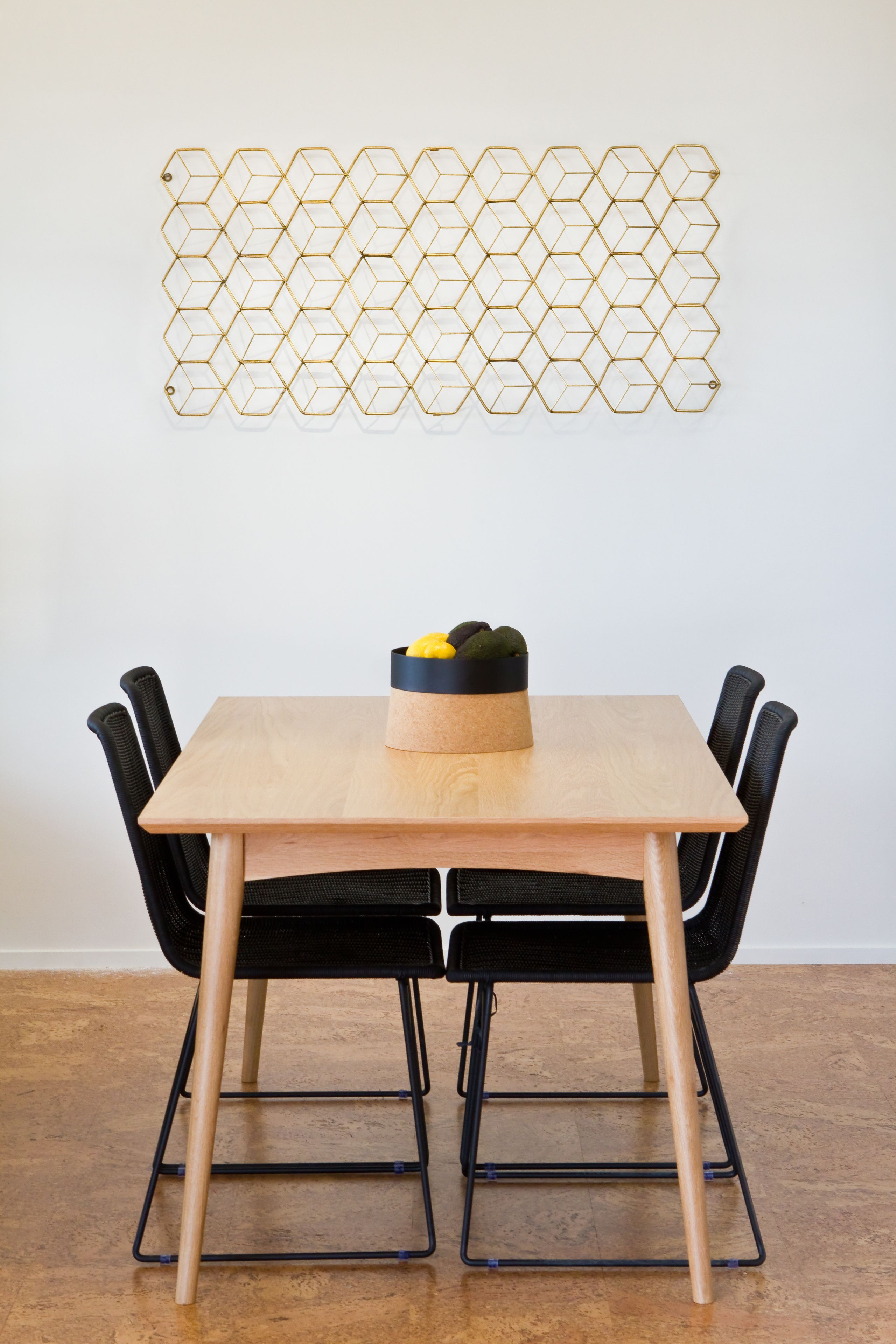 Un tavolo da pranzo con quattro sedie nere, un elemento decorativo a forma esagonale al muro e una piccola pianta sul tavolo.
