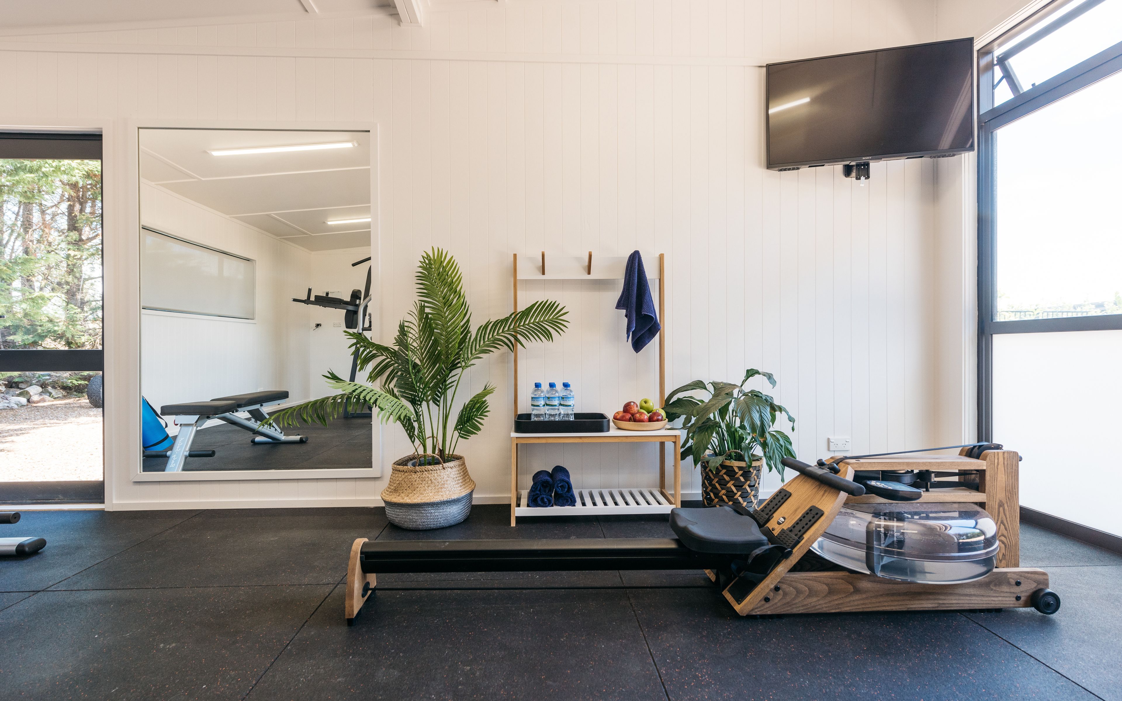 A gym with exercise equipment, a water station, and a television mounted on the wall.