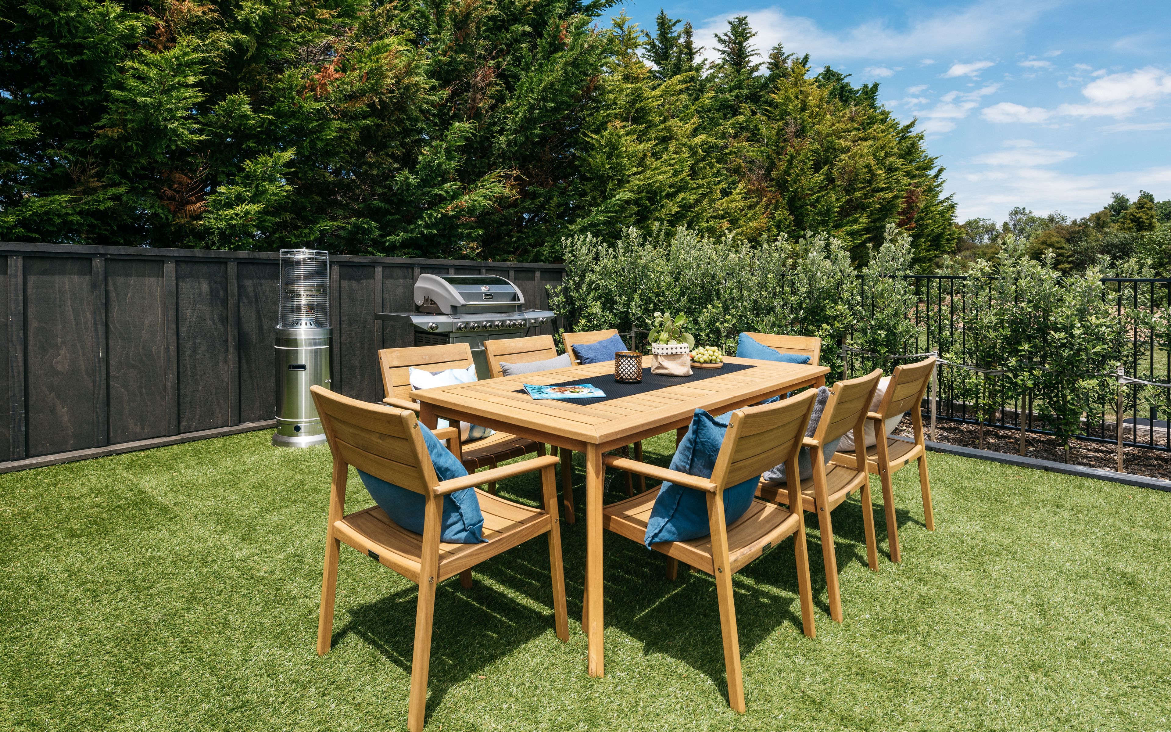 A wooden table with chairs in a backyard, a barbecue grill, and a tall heater.