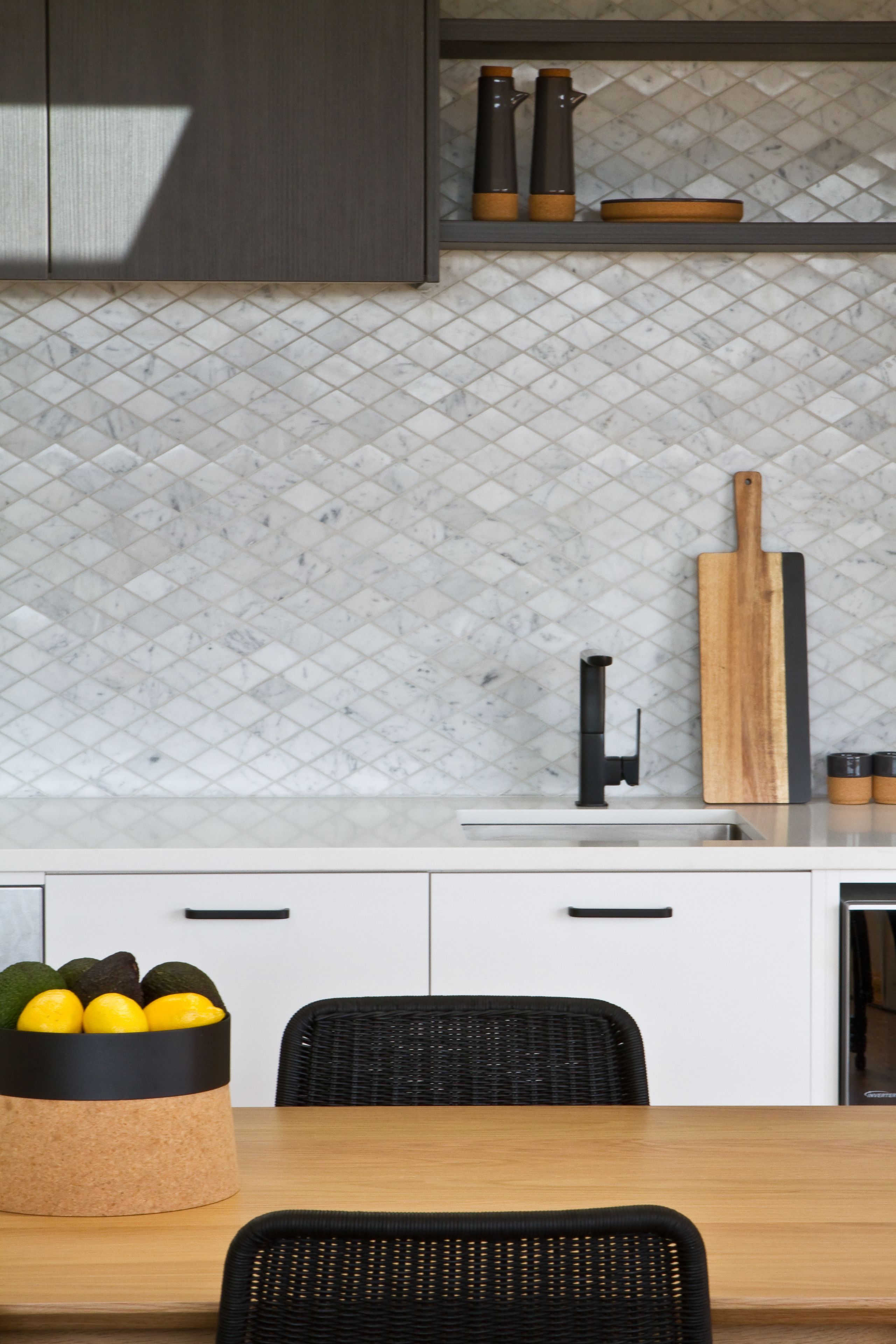 A modern kitchen with white cabinets, a marble backsplash, a wooden cutting board, and a bowl of lemons.