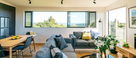 A modern living room with a dining area, large windows, and a view of the outdoors.