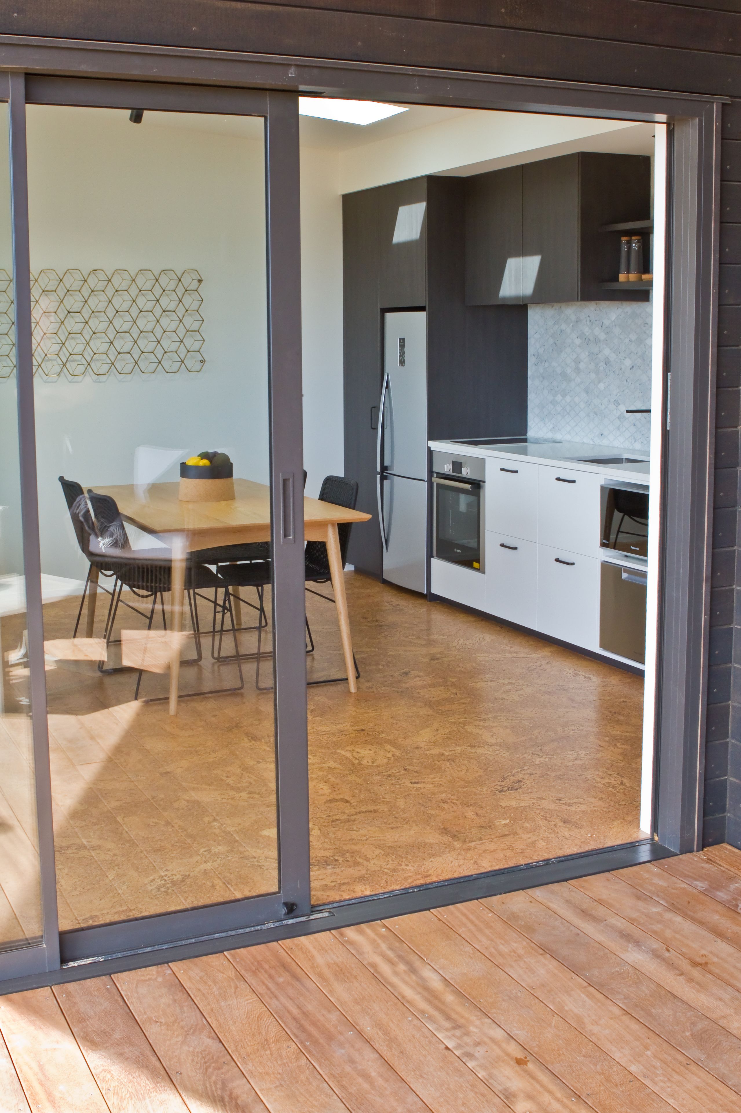 A modern kitchen with white cabinets, a wooden dining table, and a glass sliding door leading to an outdoor area.