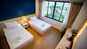 A hotel room with two beds, a desk with a lamp, a remote control, and a view of the city through the window.