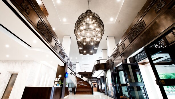 Um hall amplo com um lustre imponente, uma escadaria e um balcão de recepção.