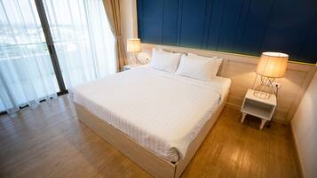 Habitación de hotel moderna con una cama grande, dos mesitas de noche con lámparas, vistas a través de un ventanal amplio y suelo de madera.