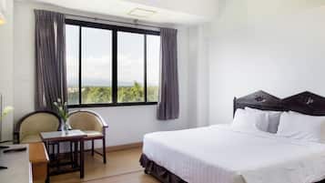 A hotel room with a bed, a desk, a chair, and a window with curtains.