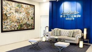 Um saguão de hotel com uma grande pintura abstrata, um sofá macio, uma mesa de centro e uma parede azul decorativa com o nome do hotel.