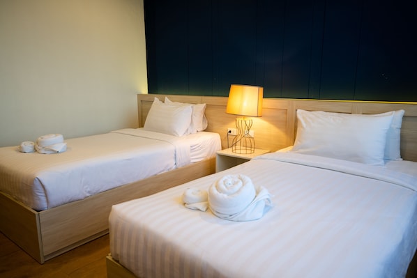 Habitación de hotel con dos camas individuales, cada una con ropa blanca y toallas. Entre las camas, una mesita de noche con lámpara.