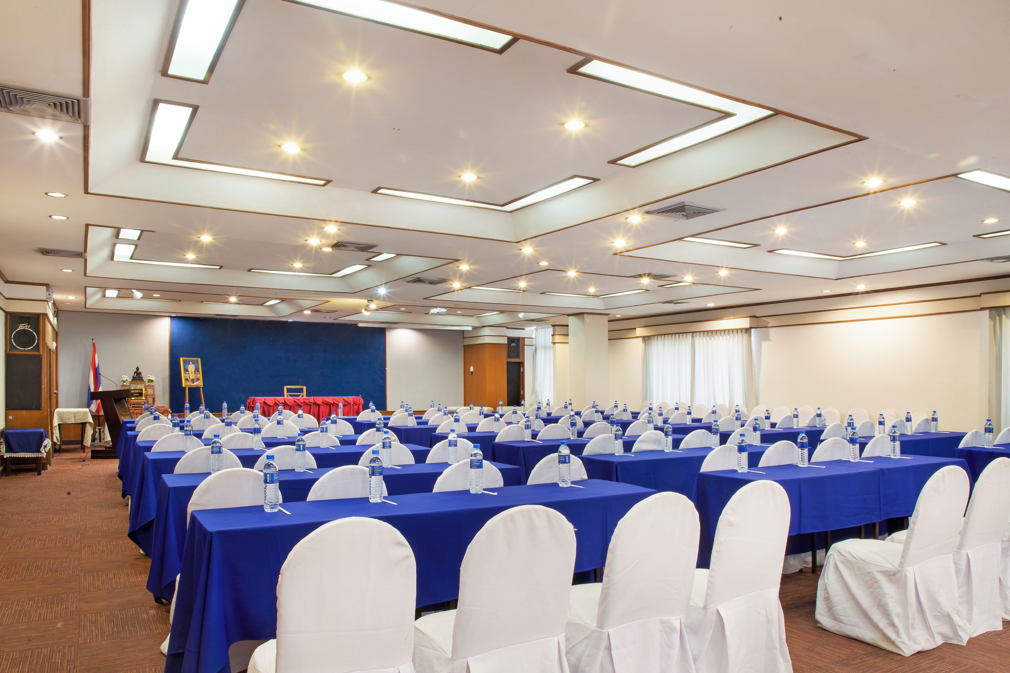 A conference room with rows of tables, white chairs, and blue tablecloths.