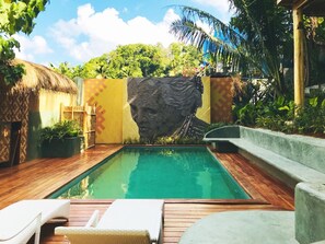 Un área de piscina con un mural, terraza de madera y vegetación circundante.