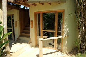 A wooden staircase leading to a door with a glass panel, surrounded by plants and a concrete floor.