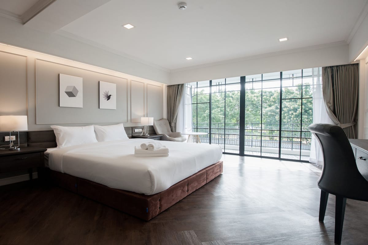 Un dormitorio de hotel moderno con una cama grande, mesitas de noche, un escritorio y vistas a zonas verdes a través de amplios ventanales.