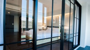 Una habitación de hotel moderna con una cama grande, una mesita de noche y un ventanal con vistas a la ciudad.