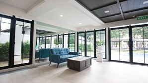 Un vestíbulo amplio con un sofá azul, una mesa de centro de mármol y grandes ventanales con vistas a una piscina y zonas verdes.