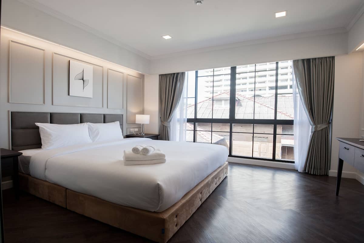 Una habitación de hotel con una cama grande, una mesita de noche, un escritorio y una ventana con cortinas.