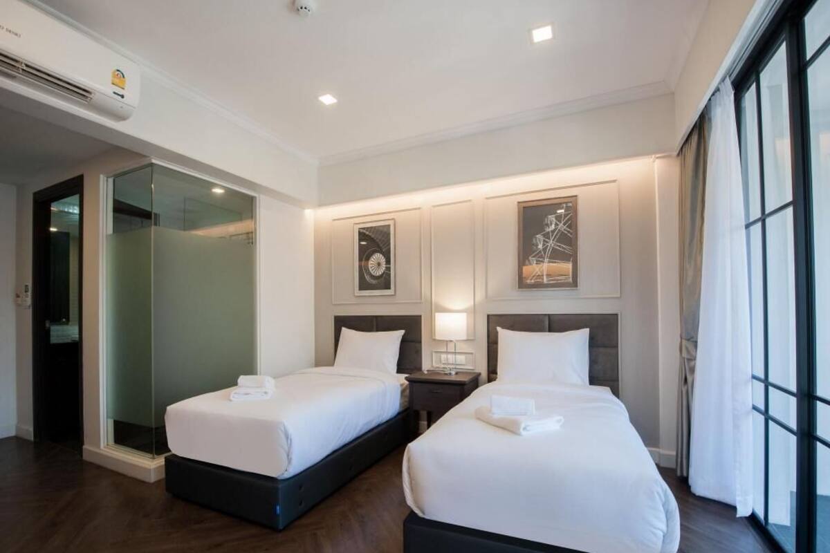 Habitación de hotel con dos camas, una puerta de vidrio y un ventanal grande.
